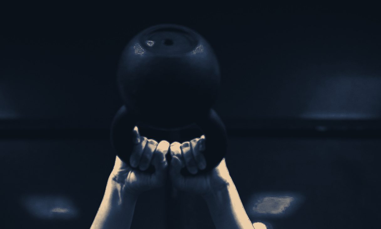 Athlete pressing a kettlebell overhead in a dark gym, hands locked out